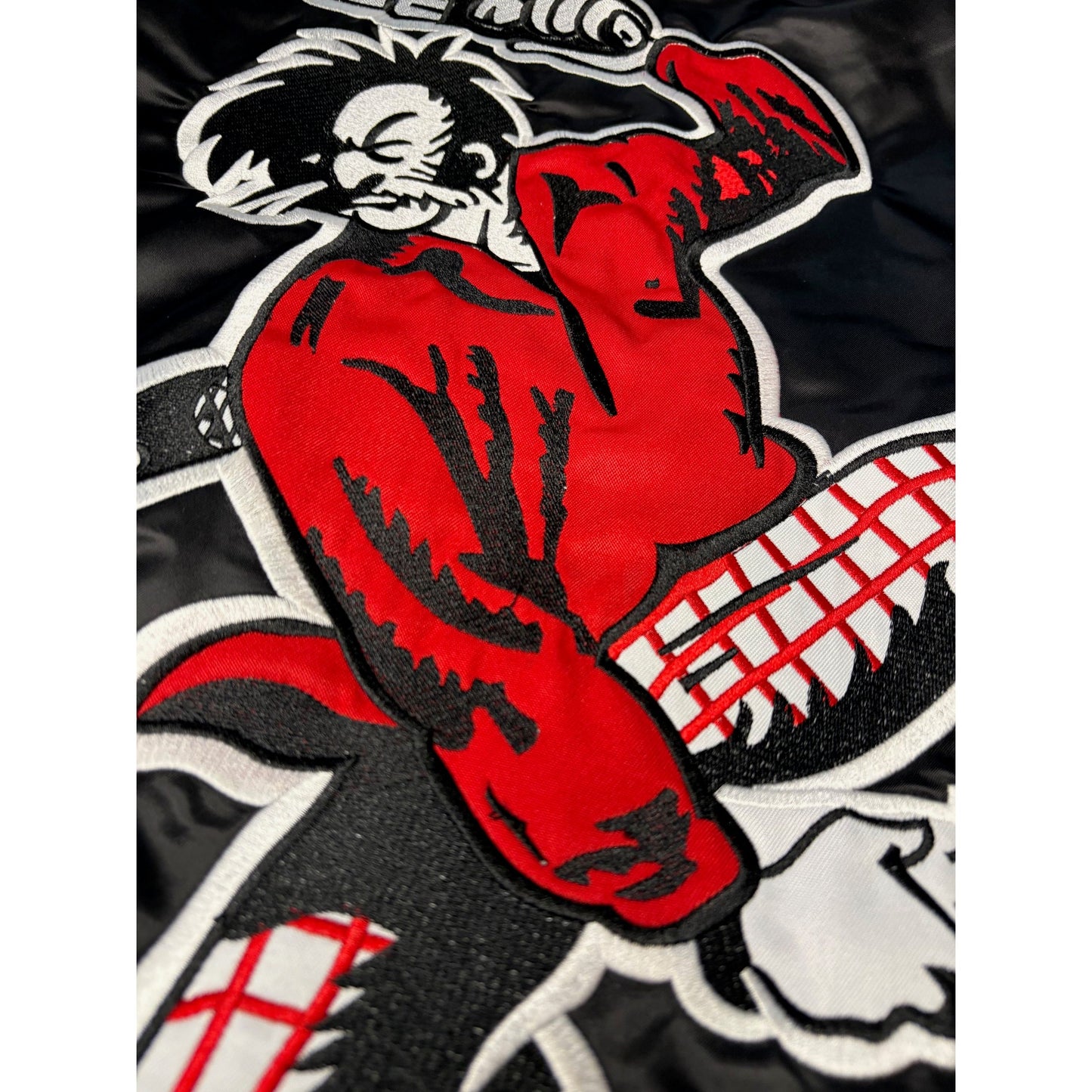 Kezar Satin Jacket - Black Jackets. Back. Close up of Prospector in red shirt and white and red checkered pants firing a pistol down between his legs while holding another pistol in his left hand over his head.