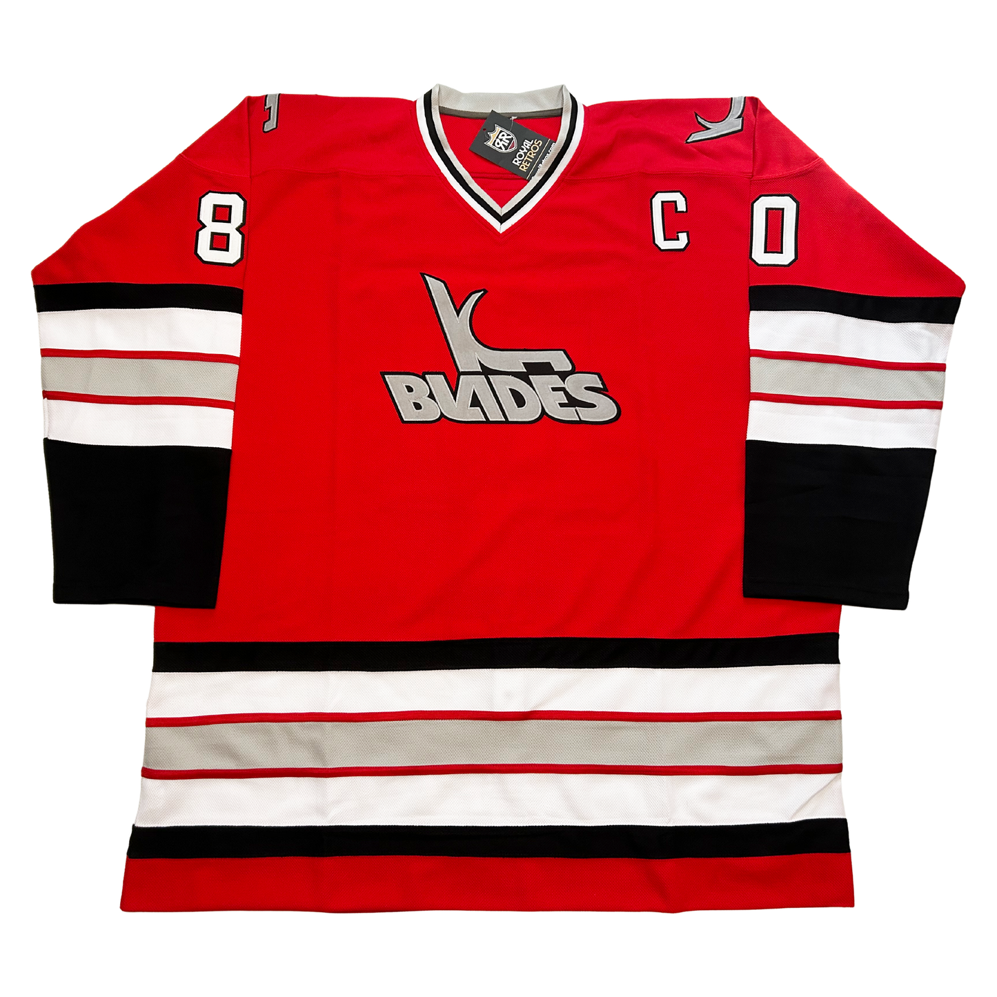Kansas City Blades hockey jersey. Red. Black, white, red, sliver, red, white bands mid-sleeve and just above waist. Black sleeve ends. White, black, and white, collar. Captain's "C" white left chest. Blades logo in silver, featuring "Blades" slanted to the left and K with a blade coming off bottom. #80 white with black trim on upper shoulders. Royal Retros