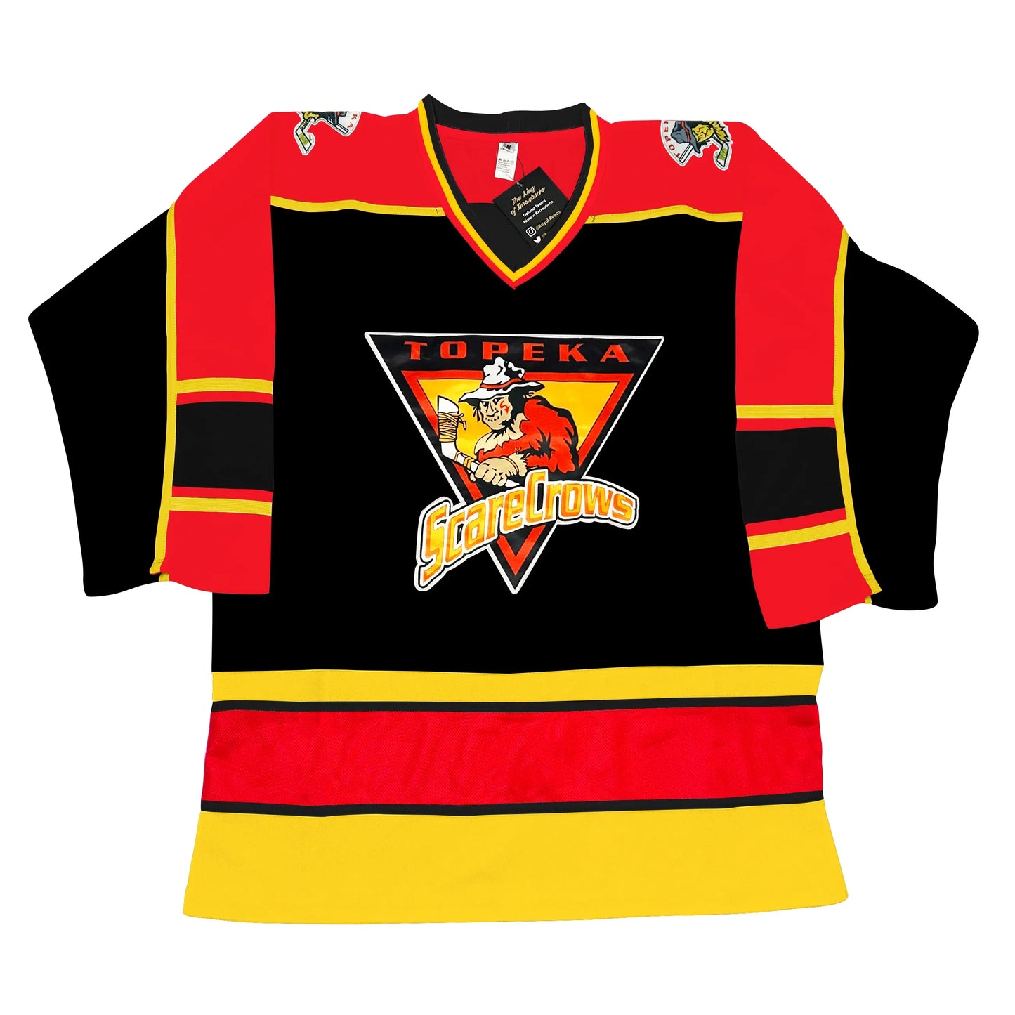 Topeka Scarecrows hockey jersey black. Red shoulders. Half black sleeves, half red, separated by a gold line. Thin gold, thin red, thick black, thin red, thin gold ban mid-sleeve. Gold, red, gold ban separated by black line at waist. Logo in center is upside down triangle outlined in white. TOPEKA in red above a scarecrow holding a hockey stick over a gold triangle outlined in red. Stylized SCARECROWS arched across bottom of main Triangle. Royal Retros