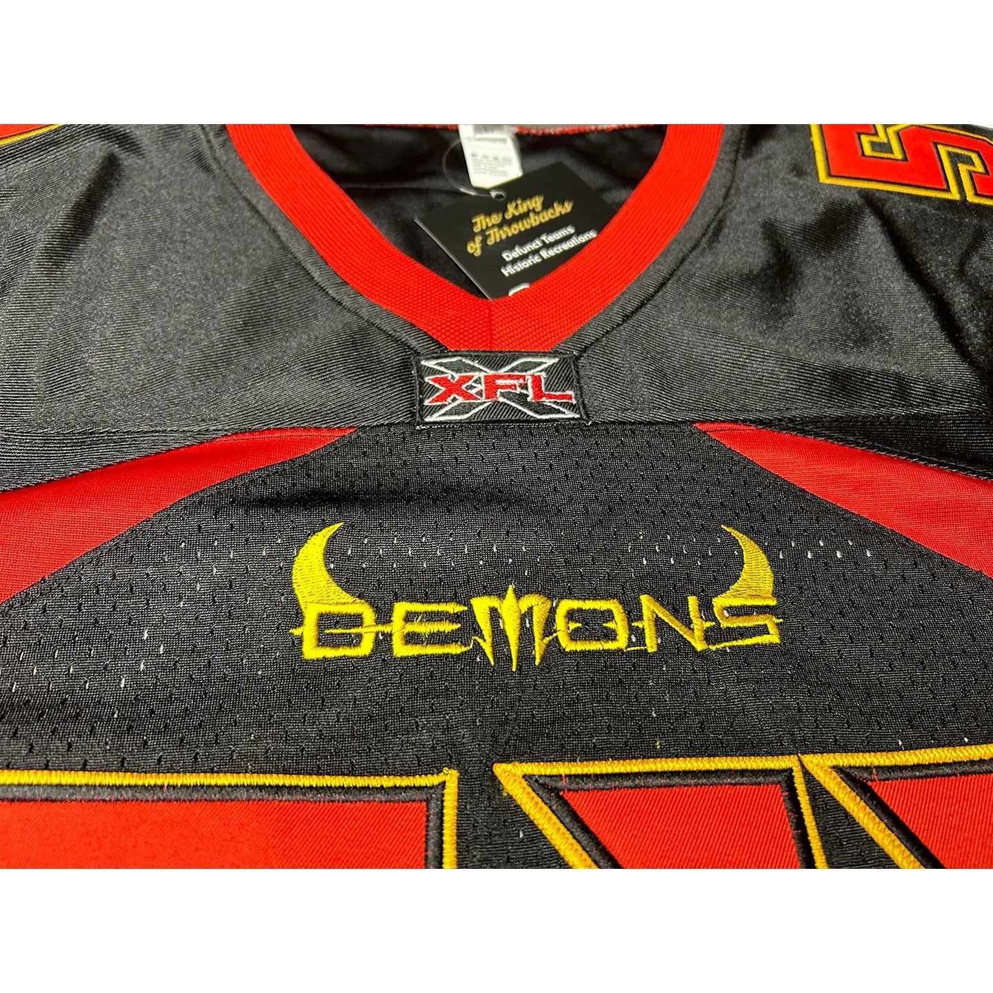 San Francisco Demons remix jersey. Black. Close-up of Demons above numbering. Red trim on sides. Red trim on neck. Red lower sleeves. #54 in red with gold trim, large on chest. small on shoulders. Royal Retros