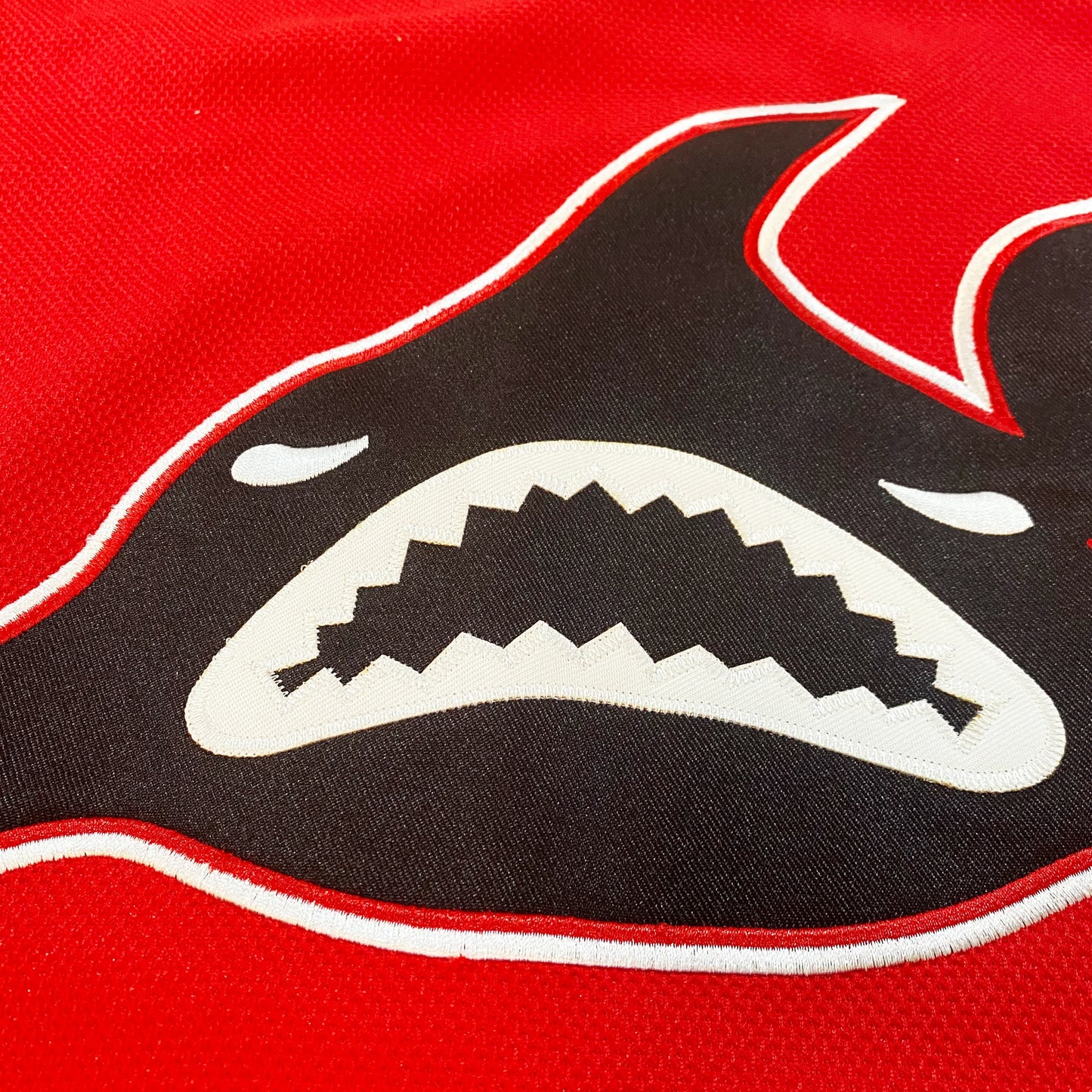 Los Angeles Sharks Jersey close-up red. Black shark with white outline, straight on, white teeth and eyes. Royal Retros