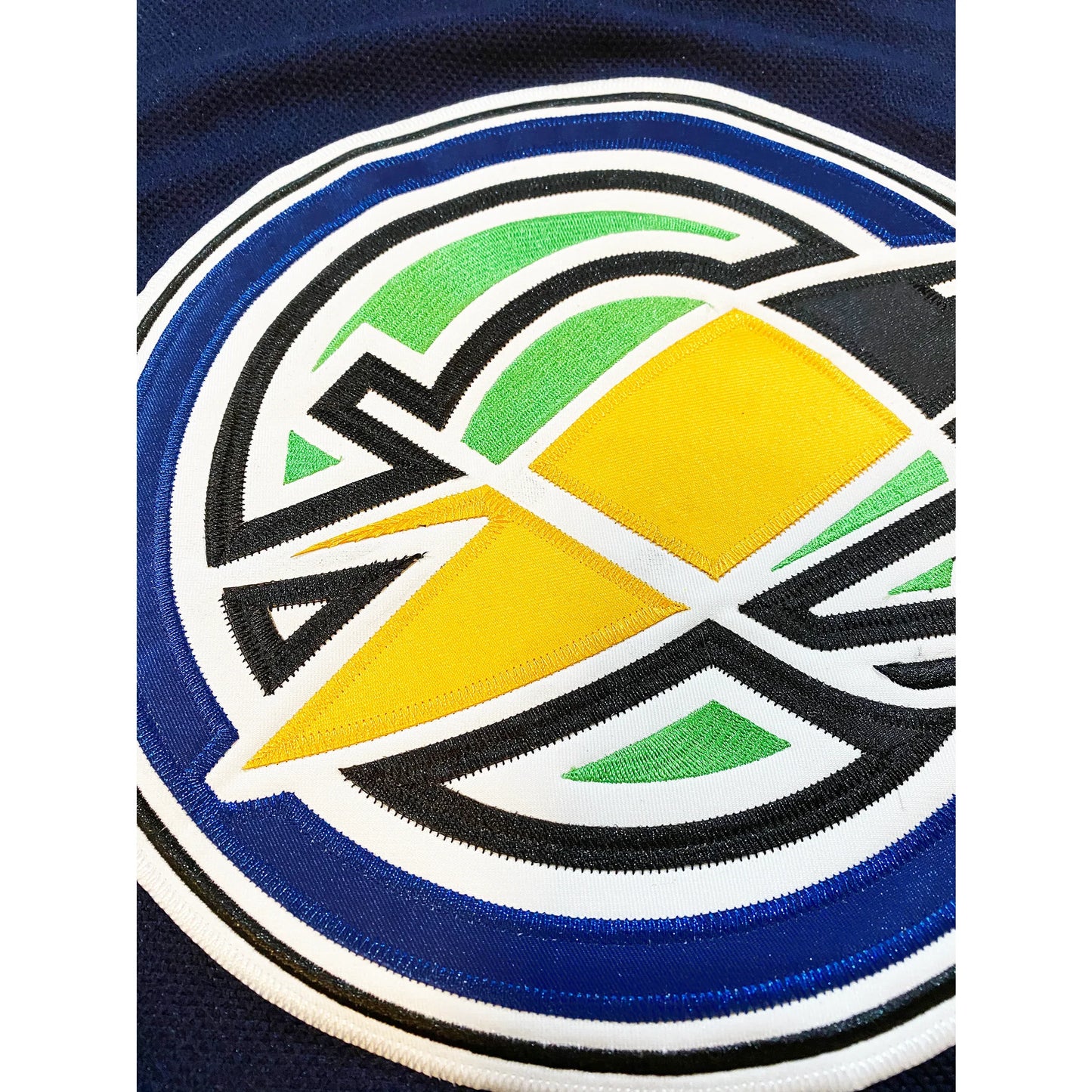 Oakland Seals hockey jersey navy blue, close-up of logo with yellow seal with black trim inside concentric circles of white, black, and royal blue. Royal Retros