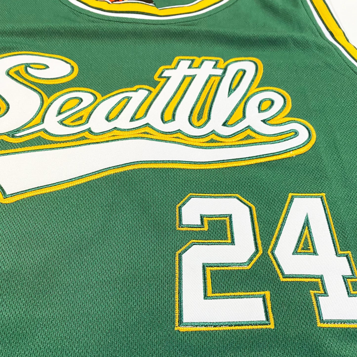 1970 Seattle Supersonics Basketball Jersey. Green with gold and white trim. Seattle in script with tail below in white with gold trim. #24 in white with gold trim. Close-up. Royal Retros
