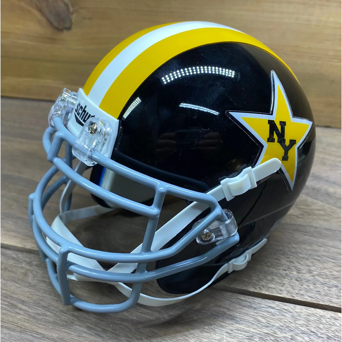New York Stars Mini Helmet. Black shell with gold and white stripes over the crown and a gray facemask. Gold star decal with "NY" in black on the side.