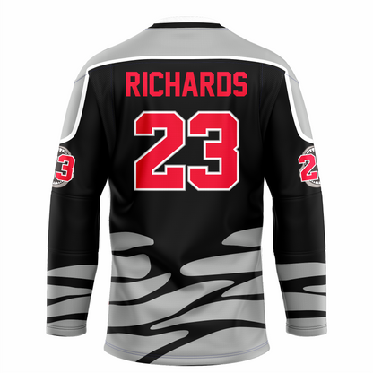Tallahassee Tiger Sharks hockey jersey. Black. Black and white collar, silver shoulders with white trim. Random silver patter at sleeve ends and around waist suggesting ocean waves. RICHARDS in red above #23 in red with white trim large on back. Royal Retros