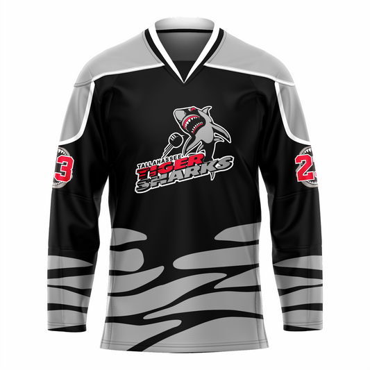 Tallahassee Tiger Sharks hockey jersey. Black. Black and white collar, silver shoulders with white trim. Random silver pattern at sleeve ends and around waist suggesting ocean waves. Logo is a shark swimming toward viewer with Tallahassee small in black with white trim above Tiger  in red and Sharks in silver. Royal Retros