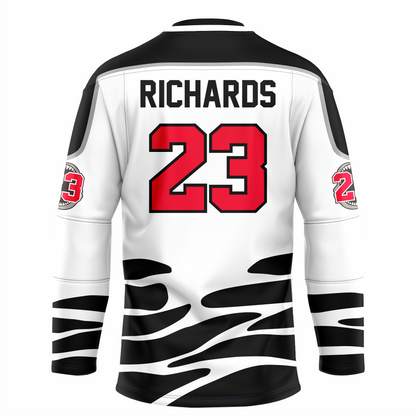Tallahassee Tiger Sharks hockey jersey. White. Black and white collar, black shoulders with silver trim. Random black pattern at sleeve ends and around waist suggesting ocean waves. RICHARDS in red above #23 in red with white trim large on back.  Royal Retros