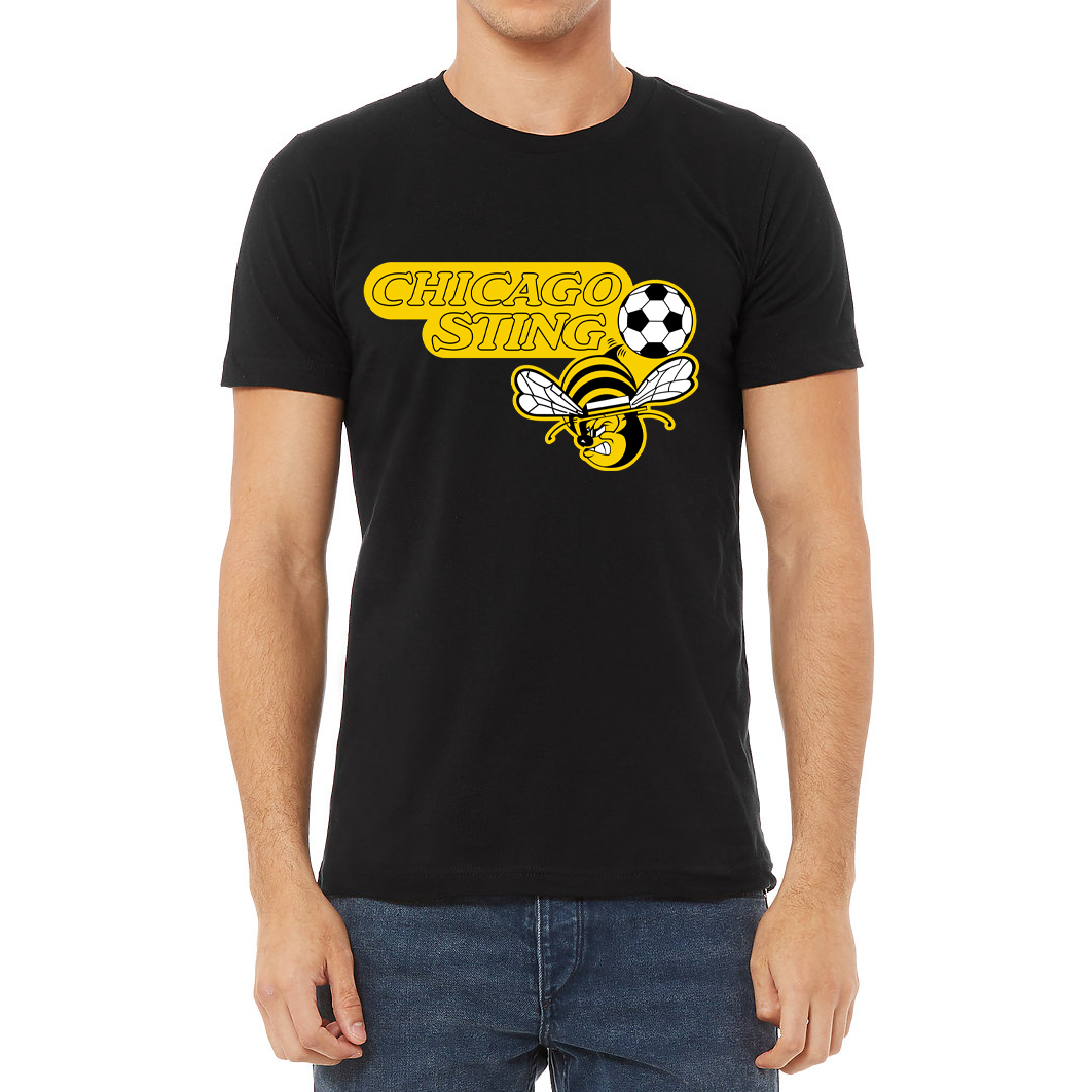 Chicago Sting T-shirt black. "Chicago" slightly over "Sting" to the left. Black and white soccer ball to the right with angry cartoon be with white wings below. Royal Retros. 