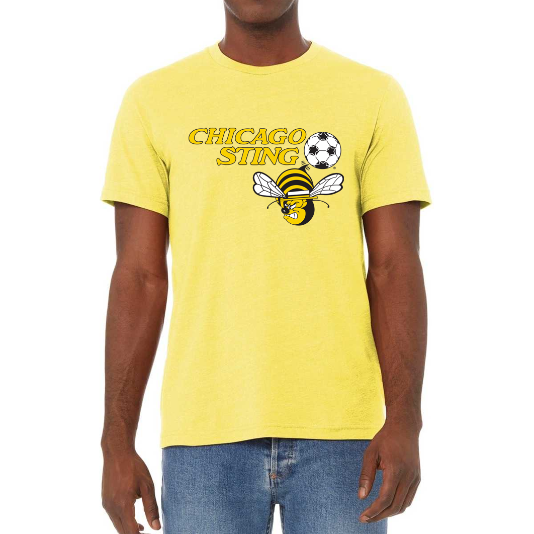 Chicago Sting T-shirt yellow. "Chicago" slightly over "Sting" to the left in gold. Black and white soccer ball to the right with angry cartoon be with white wings below. Royal Retros. 