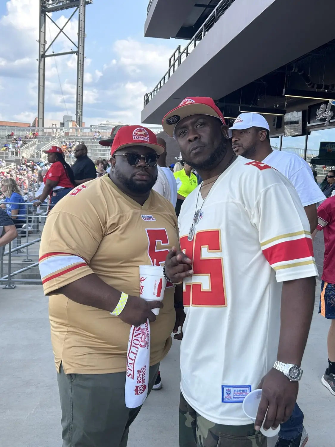 Two fans wearing custom team jerseys and hats at a stadium on gameday