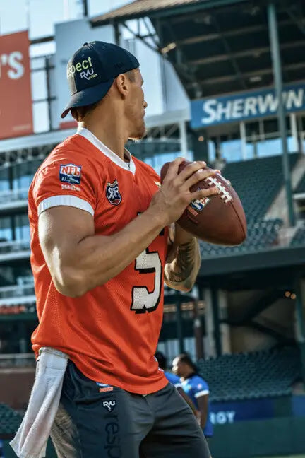 Football player throwing a pass in a custom orange jersey at a professional stadium