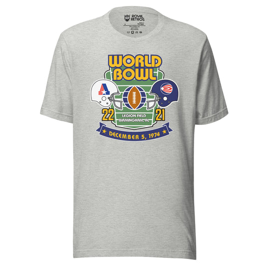World Football League World Bowl T-shirt. Gray. World in Gold above Bowl in Gold over top of vertical football field. White helmet to left with A formed by red stripes on left, blue bar on right, star at bottom. On the right, blue helmet with white dot with white and red stripes leading a way. between helmets is a football vertical with partial globe quarters on blue on wither side. 22 in gold below white helmet. 21 in gold below blue helmet. Between numbers on bottom of football field Legion Field.