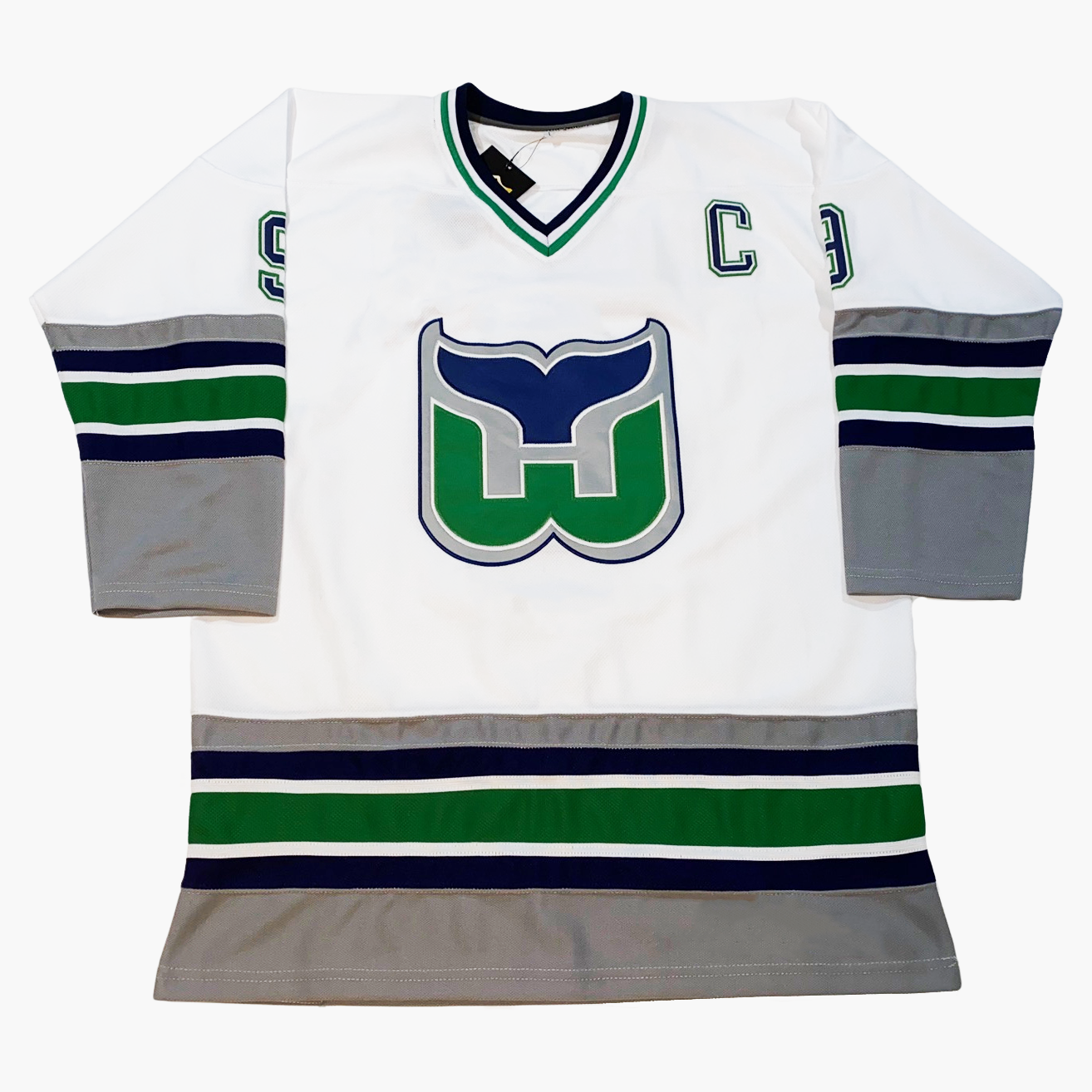 1994 Whalers Jersey white with silver, blue, white, and green trim on sleeves and waist. Captain C in green with blue trim, W whale tail logo with blue tail, green W, on gray background trimmed in blue in center of jersey Royal Retros