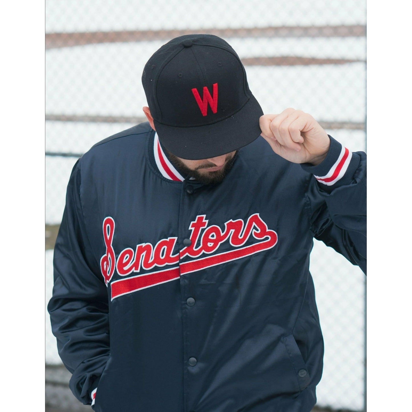 Man wearing Senators Jacket and cap. Blue jacket with white and red trim Senators script in red with white trim Royal Retros. Navy cap with red W Royal Retros
