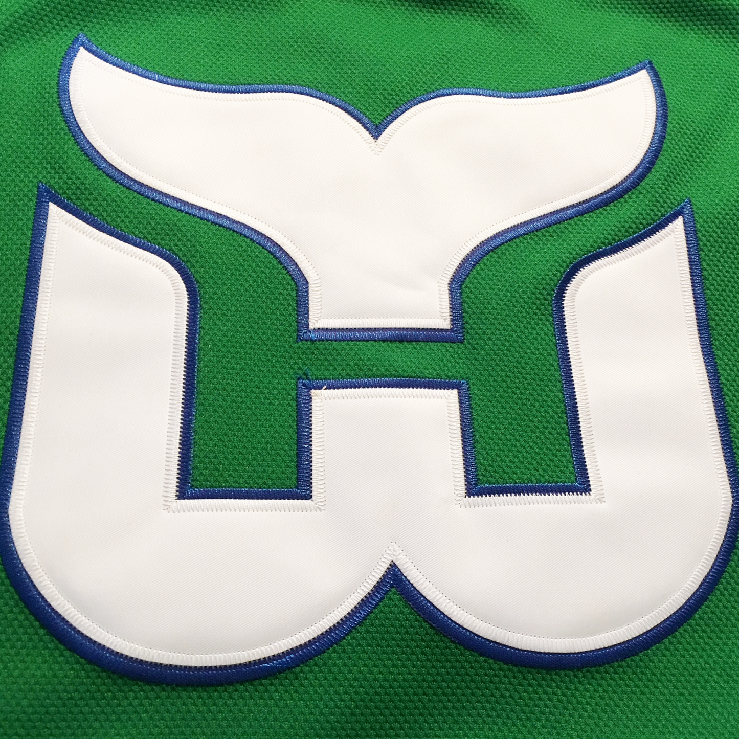 1979-91 Whalers Jersey green close-up logo of whale tail logo in white with blue trim on green jersey. Royal Retros