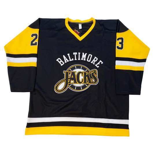 Baltimore Skipjacks jersey. Black. Gold collar. Gold upper sleeve, black lower, with black, white, gold bands mid-sleeve and around waist. Baltimore n white arched above stylized Jacks logo. Jacks in black with gold trim over white ship's wheel. #23 in black with white trim on shoulders. Royal Retros.