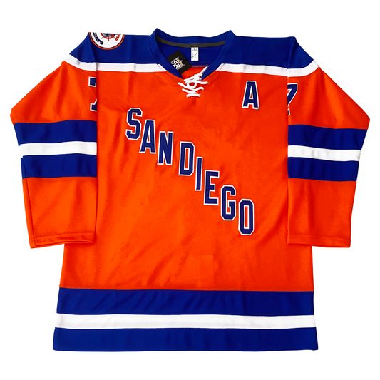 San Diego Mariners hockey jersey. Orange. Blue shoulders with white trim. Blue, white, and blue bands mid-sleeve and around waist. Co-captain A in blue with white trim on left upper chest. SAN DIEGO diagonal down left to right in blue with white trim. Logo patch on right shoulder. Royal Retros